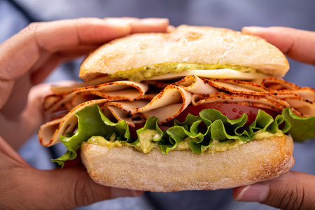 Hands holding fresh and healthy pesto turkey sandwich with white cheddar cheeseの写真素材
