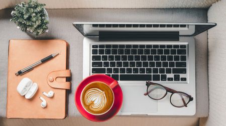 Dark office desk workspace with laptop computer, eyeglass, earphone, pen, notebook and cup of coffee
