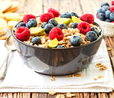 A bowl of oatmeal topped with fresh raspberries, blueberries, and lime wedges. The oatmeal is served on a rustic wooden table with a white napkin.の写真素材