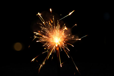 A single burning sparkler creates a dazzling display of bright sparks against a completely dark...