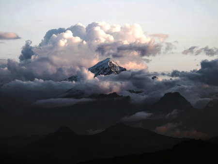 A snow-covered mountain peak dramatically rises above a sea of clouds at sunset, casting long shadows on the surrounding mountain range. The scene is serene and awe-inspiring.の写真素材