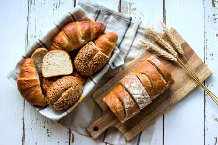 top view of breads as croissant and seeded brown cob bread slices in basket on cloth and crusty...