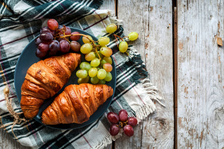 top view of croissants with grape in plate on plaid cloth on wooden background with copy spaceの写真素材