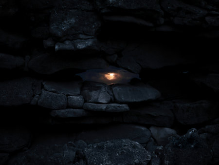 A vibrant sunset is visible through a small gap in a dark, rough stone wall. The contrast between...