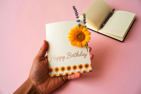 A person's hand holds a birthday card adorned with a sunflower and lavender sprigs. The card has a rose gold Happy Birthday message and a sunflower border.の写真素材
