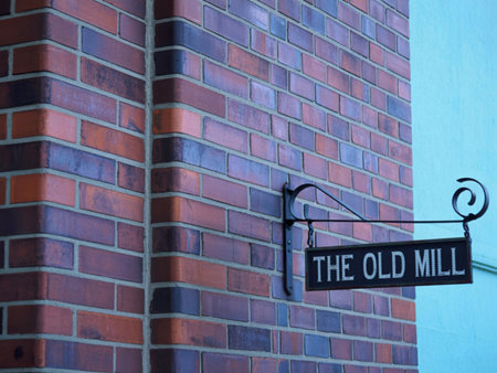 A black sign reading The Old Mill hangs on a brick wall. The sign is attached to an ornate metal bracket. The brickwork is a mix of reddish-brown hues.の写真素材