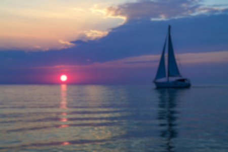 A sailboat glides across a tranquil ocean under a vibrant sunset sky. The sun is a large, reddish...