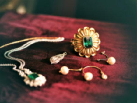A luxurious display of gold and silver jewelry featuring emeralds and pearls rests on a rich burgundy velvet fabric. The pieces include necklaces, earrings, and a statement ring.の写真素材