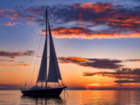 A sailboat is silhouetted against a vibrant sunset, its sails catching the last rays of light. The...