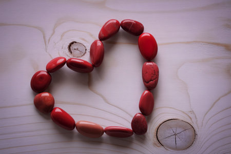 Smooth, red Mookaite Jasper stones arranged in the shape of a heart on a light wood background. The...
