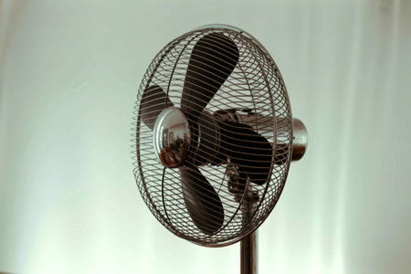A close-up shot of a vintage-style stand fan with a metallic finish and three dark blades. The fan is set against a neutral background.の写真素材