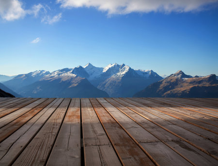 A weathered wooden deck provides a foreground to a stunning vista of snow-covered mountain peaks under a clear blue sky. The scene evokes serenity and adventure.の写真素材