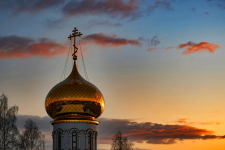 A gleaming golden dome, topped with an ornate cross, sits atop a white church against a vibrant sunset sky. The colors are warm and inviting.の素材