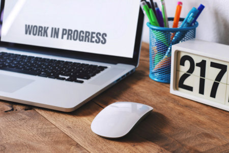 A laptop displaying Work in Progress sits on a wooden desk with a wireless mouse, pen holder, and a...