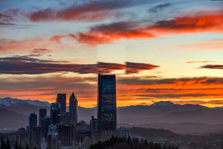 A vibrant sunset casts warm hues across a city skyline, featuring prominent skyscrapers and a distant mountain range. The City Lights tower is illuminated.の写真素材