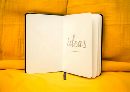 A blank notebook lies open on a yellow surface, with the word 'ideas' elegantly handwritten on one...