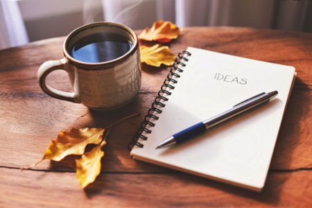A steaming mug of coffee sits beside a notebook with the word IDEAS written on it, accompanied by autumn leaves on a wooden table.の写真素材