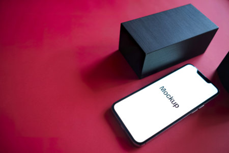 A modern smartphone displaying a mockup screen rests beside a sleek black rectangular box on a...