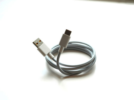 A white USB to USB-C charging cable is neatly coiled on a bright white surface, showcasing its...