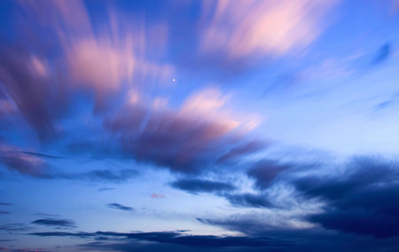 A long exposure captures the movement of clouds across a twilight sky. Streaks of pink and white...