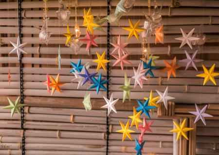 A vibrant display of multi-colored origami stars suspended against a textured bamboo backdrop, creating a festive and whimsical atmosphere.の素材
