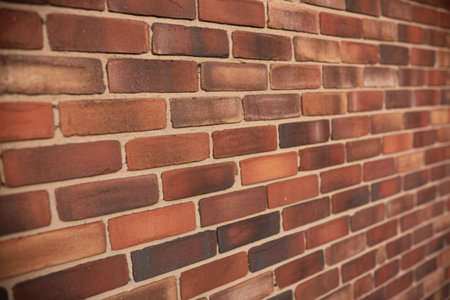 A detailed view of a brick wall, showcasing the varied tones of red, brown, and darker shades. The...