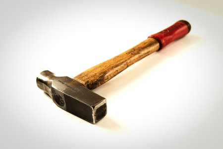 This image showcases a vintage, hand-forged hammer with a worn wooden handle and a red grip. The metal head displays the inscription "HAND FORGED" and a circular logo.の写真素材