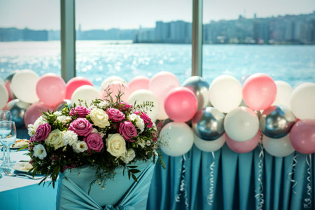 A beautiful bouquet of pink and white roses sits on a table draped in blue fabric, adorned with a festive display of pink, white, and silver balloons.の写真素材