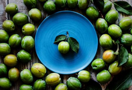 top view of an empty blue plate and sour green plums arranged around on wooden backgroundの写真素材