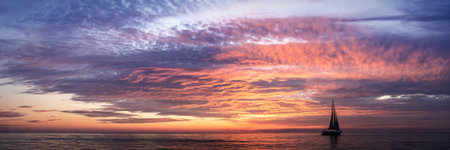 A lone sailboat glides across a calm ocean under a breathtaking sunset. The sky is filled with...