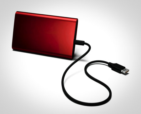 A sleek, red external hard drive is connected to a black USB cable. The device is positioned on a clean white surface, highlighting its modern design and connectivity.の写真素材