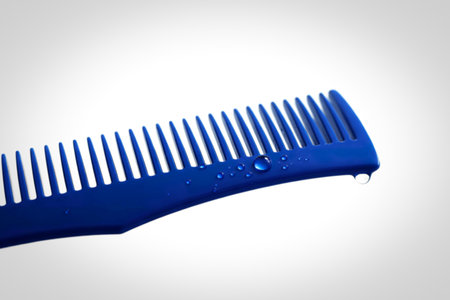 A close-up, isolated shot of a blue plastic comb featuring several clear water droplets on its...