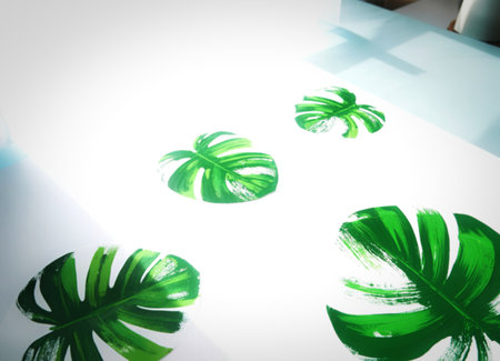 Several stylized green monstera leaves are arranged on a clean white background. Sunlight casts soft shadows, highlighting the textured brushstrokes of the painted leaf designs.の写真素材