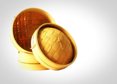 Two round, woven bamboo steamer baskets are stacked, with one lid slightly ajar, showcasing their natural texture and craftsmanship. Isolated on a white background.の写真素材