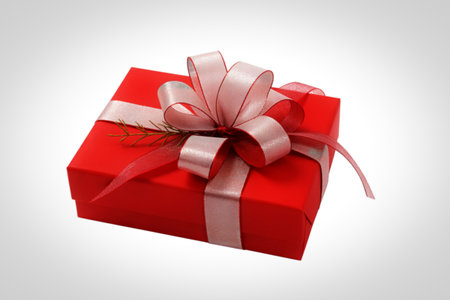 A vibrant red gift box is elegantly presented, adorned with a large, multi-layered bow made of shimmering silver and red ribbon, accented by a delicate sprig of greenery.の写真素材