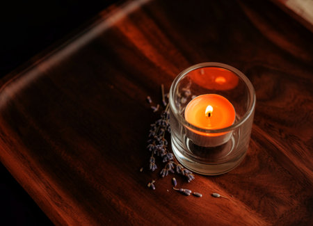 A close-up shot features a lit orange tea light candle in a glass holder, accompanied by dried...