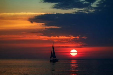 Sailboat at sunset with vibrant sky and oceanの写真素材