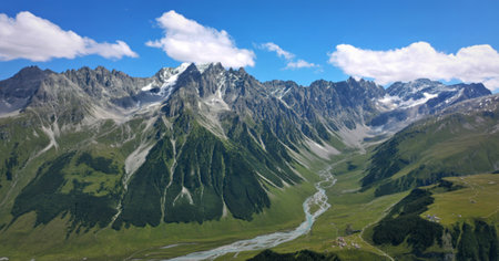 A breathtaking aerial view showcases a vast alpine mountain range, its peaks capped with snow, descending into a verdant valley carved by a meandering river.の写真素材