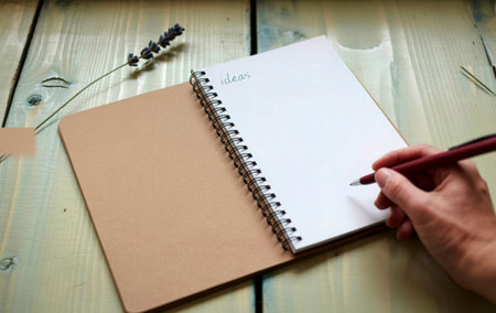 A close-up shot shows a hand holding a pen, poised to write in a blank notebook. The word ideas is...