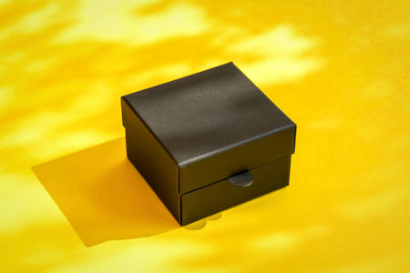 Small black gift box on yellow background with sunlight shadowsの写真素材
