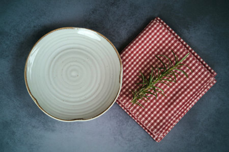 An overhead view showcases a rustic, off-white ceramic plate with concentric rings next to a folded...