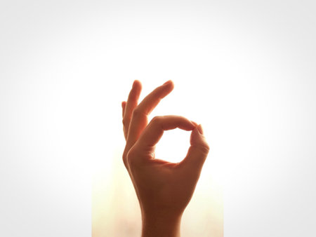 A close-up shot of a human hand, illuminated from behind, forming the 'OK' sign. The fingers are gently curved, creating a perfect circle of light.の写真素材