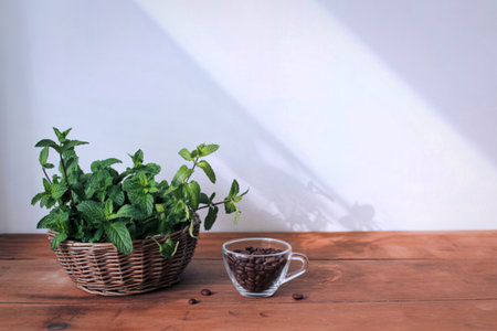 A wicker basket filled with vibrant green mint sits beside a small glass cup brimming with dark roasted coffee beans on a rustic wooden surface.の写真素材