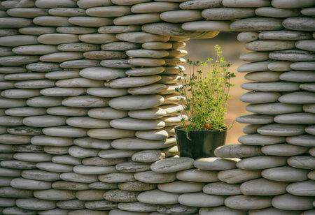 A wall constructed from smooth, rounded river stones features an arched opening. A small potted plant with green foliage is placed within this opening, adding a touch of nature.の写真素材