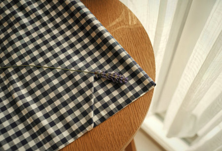 A close-up shot shows a dark blue and white gingham fabric draped over a round wooden table. A...