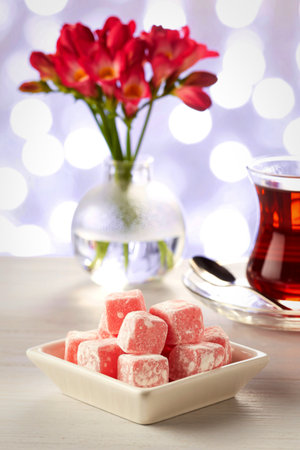 A close-up of pink Turkish Delight served with a glass of dark tea and a bouquet of red flowers.の写真素材