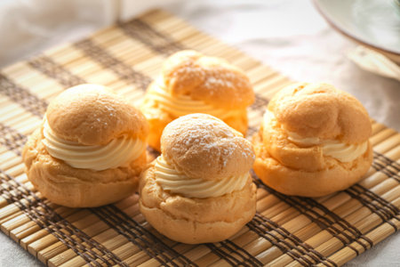 Four golden brown cream puffs filled with creamy filling are artfully arranged on a textured plaid napkin, dusted with powdered sugar.の写真素材
