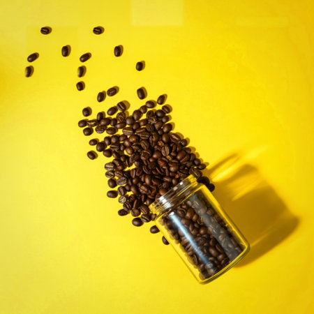 A glass bottle tipped over, spilling roasted coffee beans onto a vibrant yellow surface, creating a dynamic composition with strong shadows.の写真素材