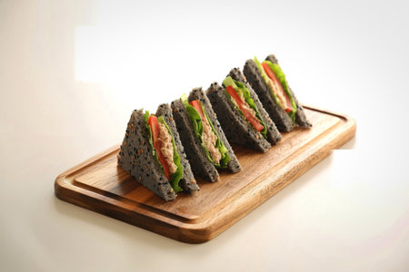 Four neatly cut club sandwiches, layered with various fillings, are presented on a rustic wooden cutting board against a plain background.の写真素材