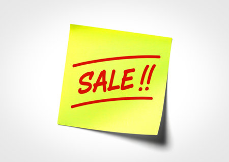A bright yellow sticky note with bold red lettering that reads "SALE!!" is attached to a white background, casting a subtle shadow.の写真素材